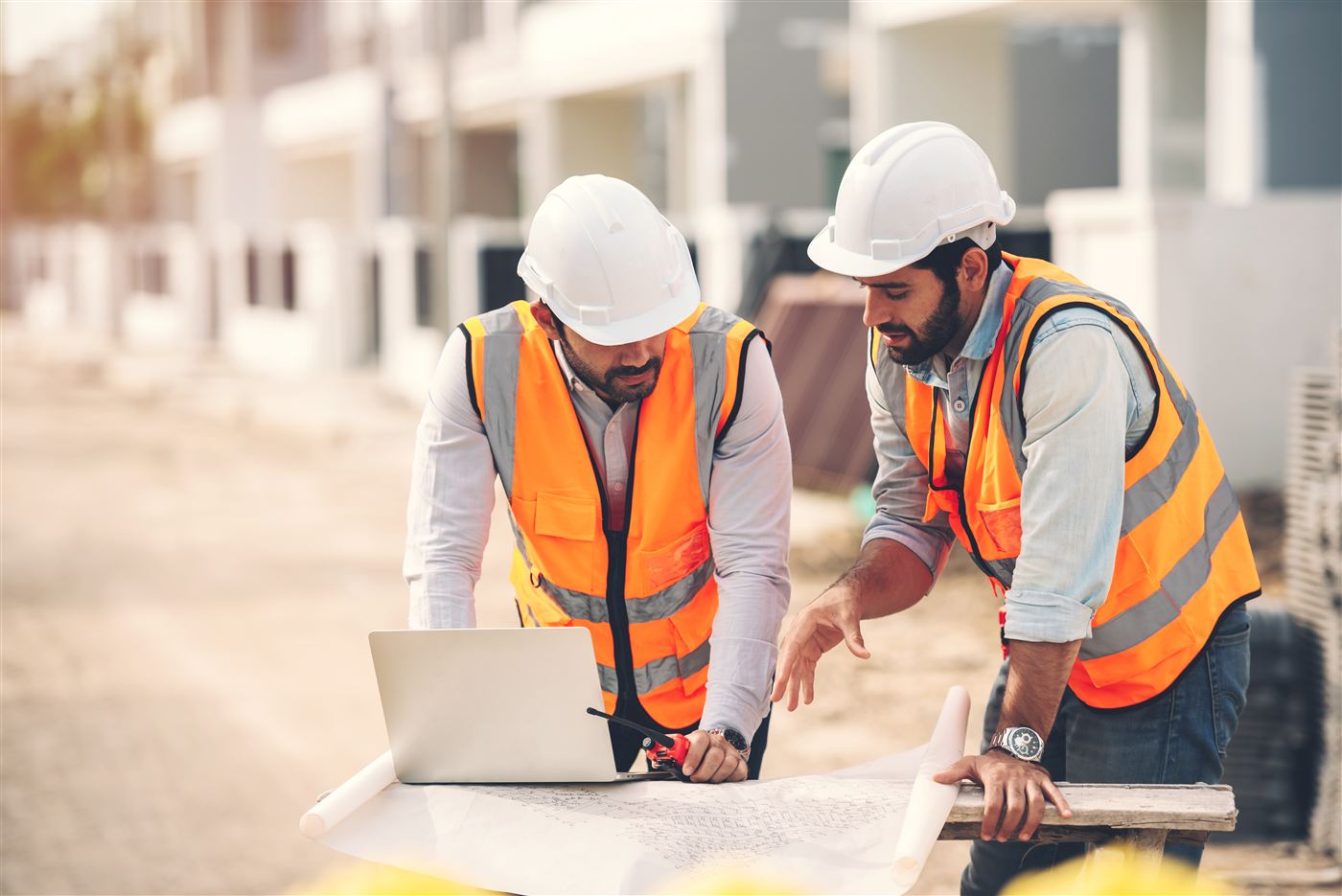 Ingenieros revisando planos estructurales frente a un conjunto de edificaciones existentes