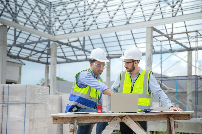 Dos ingenieros revisando un modelo estructural en una laptop durante una visita de obra